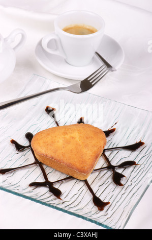 Piccola casa a forma di cuore torta servito su una lastra di vetro decorata con topping di cioccolato. Foto Stock