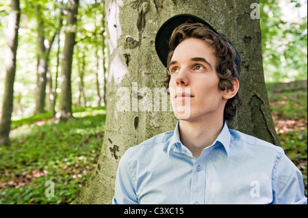 Giovane uomo seduto davanti a un albero nel bosco Foto Stock