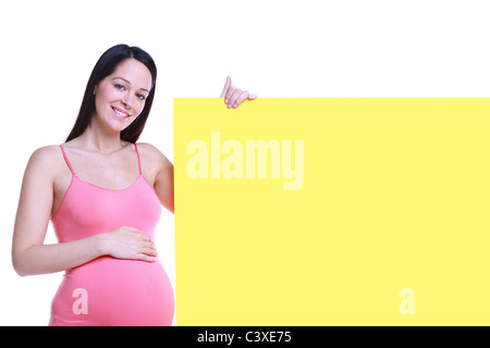 Foto di un attraente brunette donna che è di 32 settimane di gravidanza tenendo un cartello bianco, isolata su uno sfondo bianco. Foto Stock