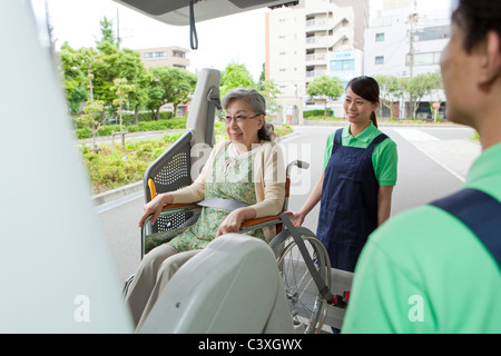 I lavoratori del settore sanitario aiutando senior donna in sedia a rotelle per arrivare in un furgone, nella prefettura di Kanagawa, Honshu, Giappone Foto Stock