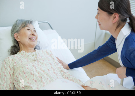 Senior donna sdraiata sul letto a parlare di infermiere, nella prefettura di Kanagawa, Honshu, Giappone Foto Stock