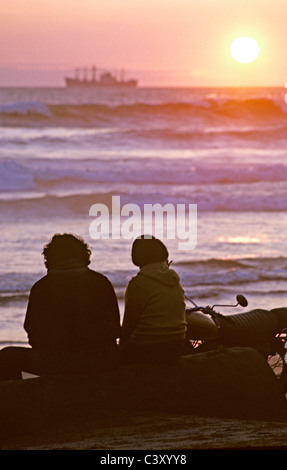 Amici e amanti sedersi e guardare la nave cargo vela verso il tramonto a Ocean Beach San Francisco California USA Foto Stock