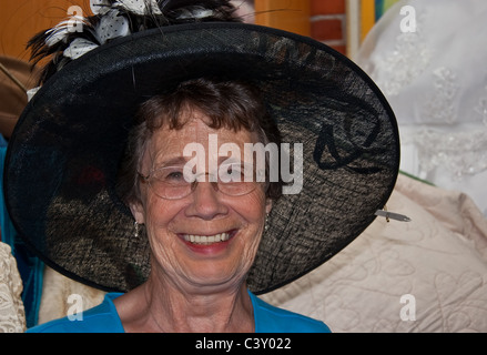 Questa felice e attiva donna anziana nei suoi anni settanta è sorridere mentre cercando su un big black hat vintage mentre lo shopping. Foto Stock