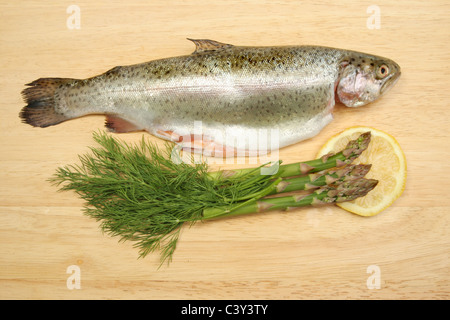 Freschi di trota arcobaleno con erbe di aneto, asparagi e limone su una tavola di legno preparazione alimentare board Foto Stock