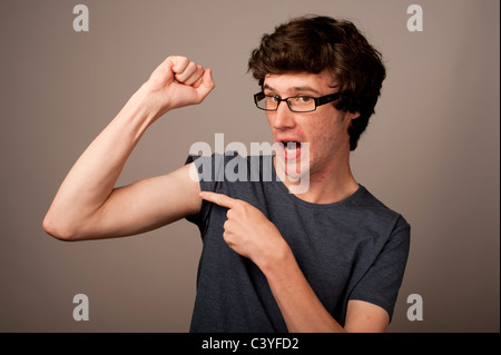 Un macchie di fronte debole debole geek nerd giovane con sottili bracci che indossano occhiali flettendo i suoi muscoli REGNO UNITO Foto Stock