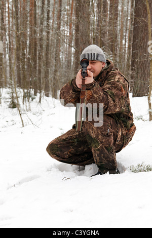 Hunter di camuffamento di mira con il fucile da cecchino a foresta d'inverno. Foto Stock