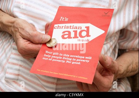 Donna che mantiene la donazione di una moneta per una raccolta di beneficenza busta per Christian Aid settimana Foto Stock