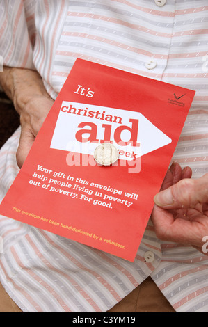 Donna che mantiene la donazione di una moneta per una raccolta di beneficenza busta per Christian Aid settimana Foto Stock