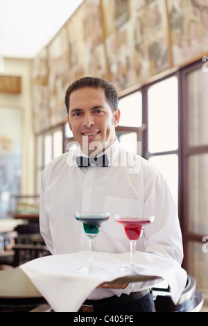 Cameriere ispanica che serve adulto giovane al tavolo nel ristorante e guardando la fotocamera. Sagoma orizzontale, vista frontale, vita fino Foto Stock