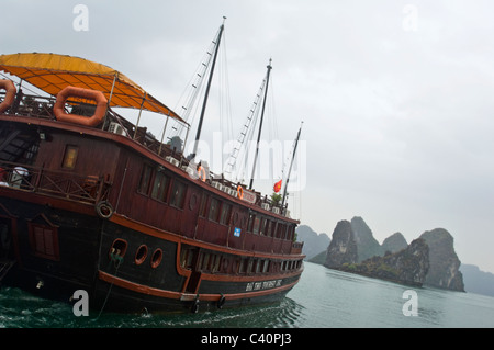 Vista orizzontale di pietre calcaree carsiche (rocce) nella baia di Halong e una tradizionale Giunca in legno usato per le guide di giro in barca a vela è passata. Foto Stock