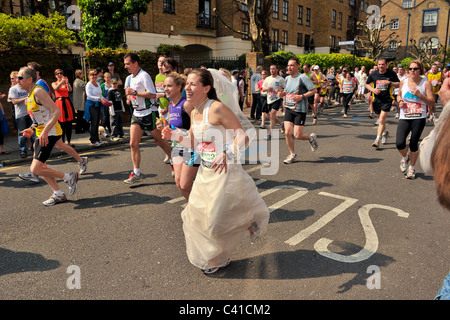 I corridori prendere parte alla Vergine 2011 London Marathon visto qui a 14 miglia in una giornata molto calda con una donna in un abito da sposa Foto Stock