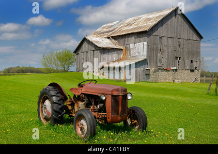 Trattori arrugginiti e vecchio fienile nel campo di erba e cielo blu nelle zone rurali di ontario canada Foto Stock