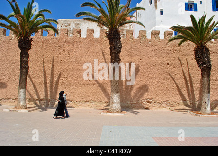 La gente a piedi passato palm ombre sul muro della città di Essaouira, Marocco Foto Stock