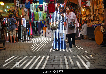 Le donne a piedi attraverso un souk di Marrakech come flussi di luce attraverso stecche nel tetto, Marocco Foto Stock