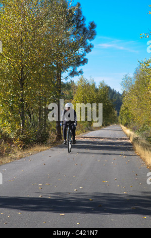 Un lone ciclista pedala lungo il sentiero del Coeur d'Alenes sull'Idaho Panhandle. Foto Stock