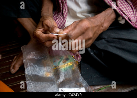 Un anziano uomo cambogiano di rotolamento è un fatto a mano sigaretta in un tempio buddista in Cambogia rurale. Foto Stock
