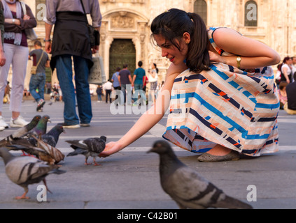 Rilassata giovane donna in abiti colorati alimenta il piccione sulla vivace piazza davanti al Duomo di Milano Foto Stock