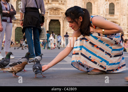 Rilassata giovane donna in abiti colorati alimenta il piccione sulla vivace piazza davanti al Duomo di Milano Foto Stock