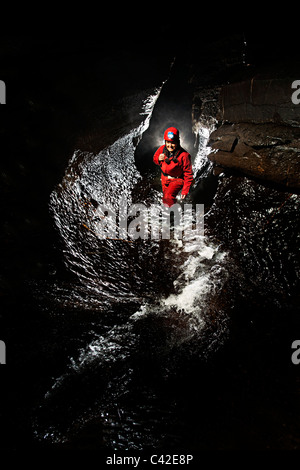 Donna speleologo nel passaggio di flusso nella grotta del Galles REGNO UNITO Foto Stock