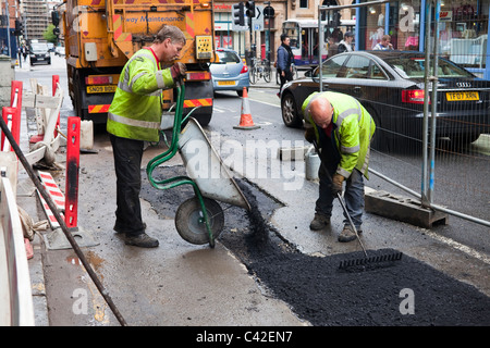 Due operai la riparazione di una superficie stradale, Glasgow, Scotland, Regno Unito Foto Stock