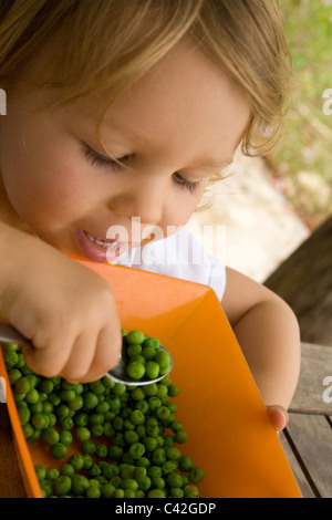 Ragazza giovane felicemente mangiare piselli Foto Stock