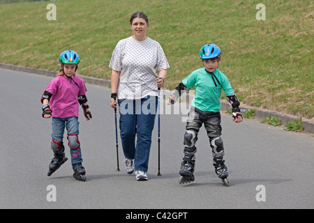 Una donna di mezza età facendo Nordic Walking, i suoi due figli piccoli pattinaggio accanto a lei Foto Stock