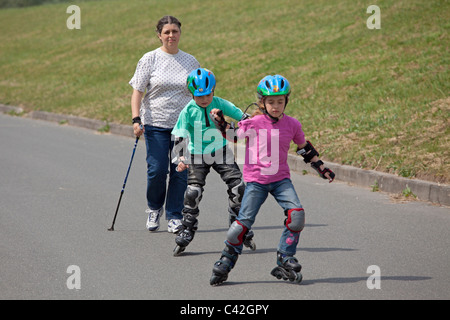 Una donna di mezza età facendo Nordic Walking, i suoi due figli piccoli pattinaggio accanto a lei Foto Stock