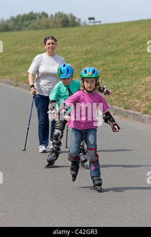 Una donna di mezza età facendo Nordic Walking, i suoi due figli piccoli pattinaggio accanto a lei Foto Stock