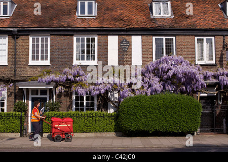 Una donna post con un carrello di consegna Consegna post a Peg Woffington in casa Teddington High Street sulla soleggiata mattina di primavera Foto Stock