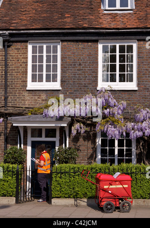 Una donna post con un carrello di consegna Consegna post a Peg Woffington in casa Teddington High Street sulla soleggiata mattina di primavera Foto Stock