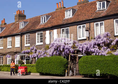 Una donna post con un carrello di consegna Consegna post a Peg Woffington in casa Teddington High Street sulla soleggiata mattina di primavera Foto Stock