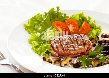 Un filet mignon-steak servita con verdure fresche e funghi saltati su una piastra bianca e sfondo bianco Foto Stock