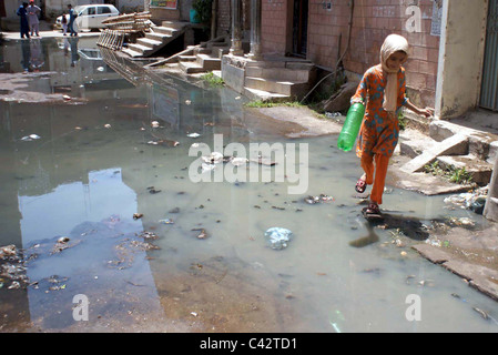 Un bambino passa attraverso il ristagno di acqua di fognatura a una strada che sta creando problemi per i residenti che mostra la negligenza Foto Stock