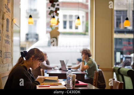 Una giovane donna siede a studiare in uno Starbucks con un caffè mentre ascolti la musica. Foto Stock