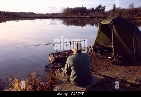 Il pescatore che gode di una buona tazza di tè sat dal lago di guardare oltre le aste a Stafford Moor pesca. Foto Stock