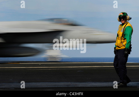 Sailor orologi la sfocatura di un aereo da caccia di decollare dal ponte della portaerei USS Carl Vinson. Foto Stock