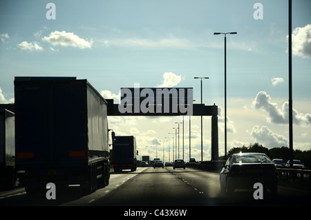 Vista del conducente dell'autostrada M62 con il traffico, lampioni e digital signage in silhouette contro un luminoso blu cielo nuvoloso Foto Stock