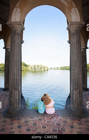 Due bambini seduti insieme sotto un arco accanto a un lago Foto Stock