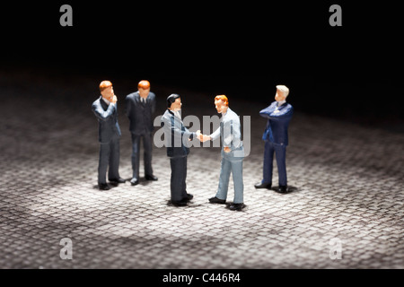 Due uomini di affari in miniatura figurine stringono le mani tra gli altri imprenditori figurine Foto Stock