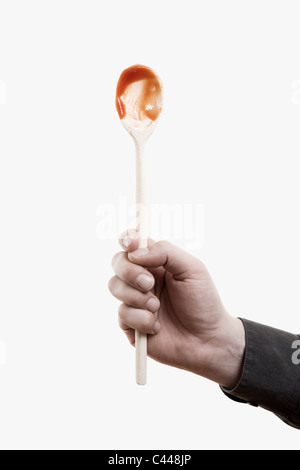 Un uomo con aloft un cucchiaio di legno con salsa rossa su di esso Foto Stock