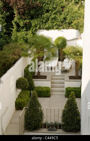 Giardino murato con terrazza, topiaria da sedie a sdraio e palme. Foto Stock