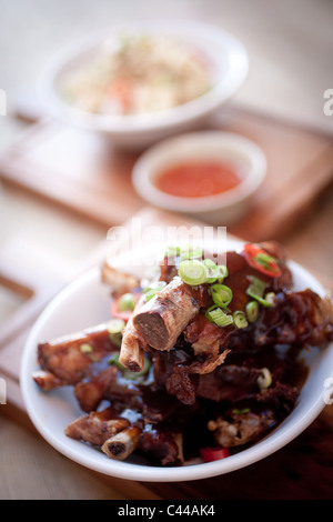 Un piatto cinese di sticky costolette di maiale servito con riso tagliatelle e peperoncino dolce salsa di immersione, cipolline Foto Stock