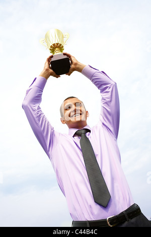 Ritratto di happy businessman sollevamento campionato di calcio con cielo nuvoloso sopra di lui Foto Stock