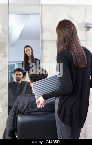 Un parrucchiere tenendo un mirror per un cliente, vista posteriore Foto Stock