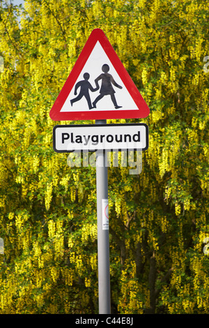 Cartello parco giochi, cartello per bambini che attraversa la strada, di fronte al colorato albero giallo laburnum a Dorset Regno Unito in aprile Foto Stock