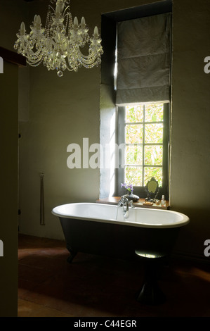 Freestanding roll-top bagno in bagno con lampadario e finestra con tenda Foto Stock