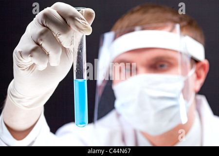 Lavoratore di laboratorio guardando il pallone con liquido blu trasparente attraverso la maschera di sicuro Foto Stock