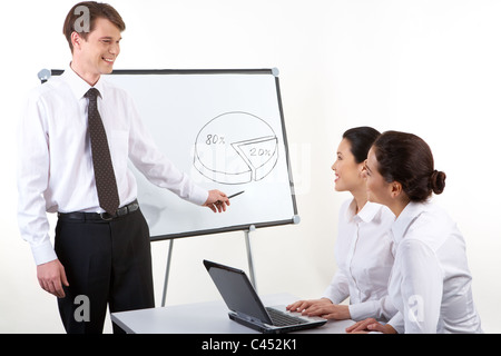 Foto di uomo felice commentando schema per i suoi colleghi che seduto alla scrivania e guardando a lui Foto Stock