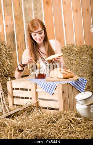 Redhead giovane donna hippie hanno la colazione sul fieno nel fienile Foto Stock