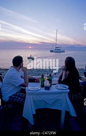 Coppia ha una romantica cena al tramonto mangia nell'isola greca di Mykonos Grecia a guardare il tramonto e barche a vela in mare Agean Foto Stock